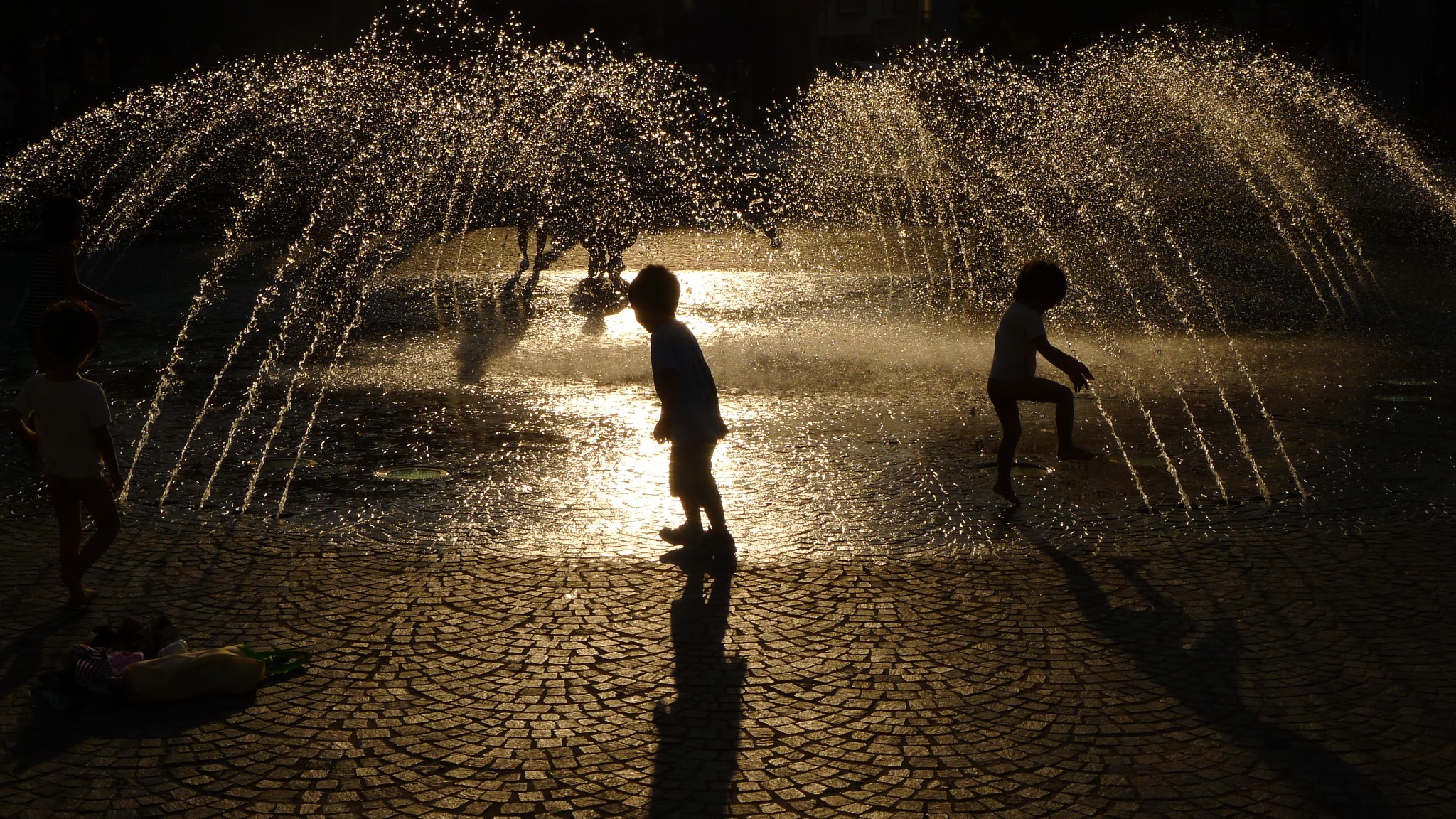 Children silhouetted in a sunlit fountain, photographed by Ching-Yi Lai